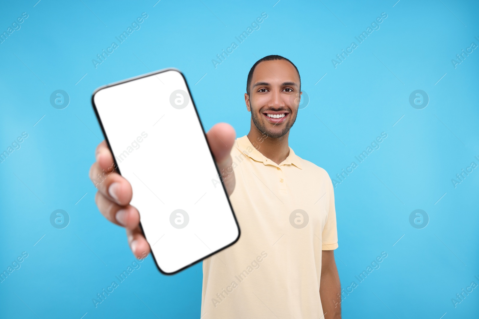 Photo of Young man showing smartphone in hand on light blue background