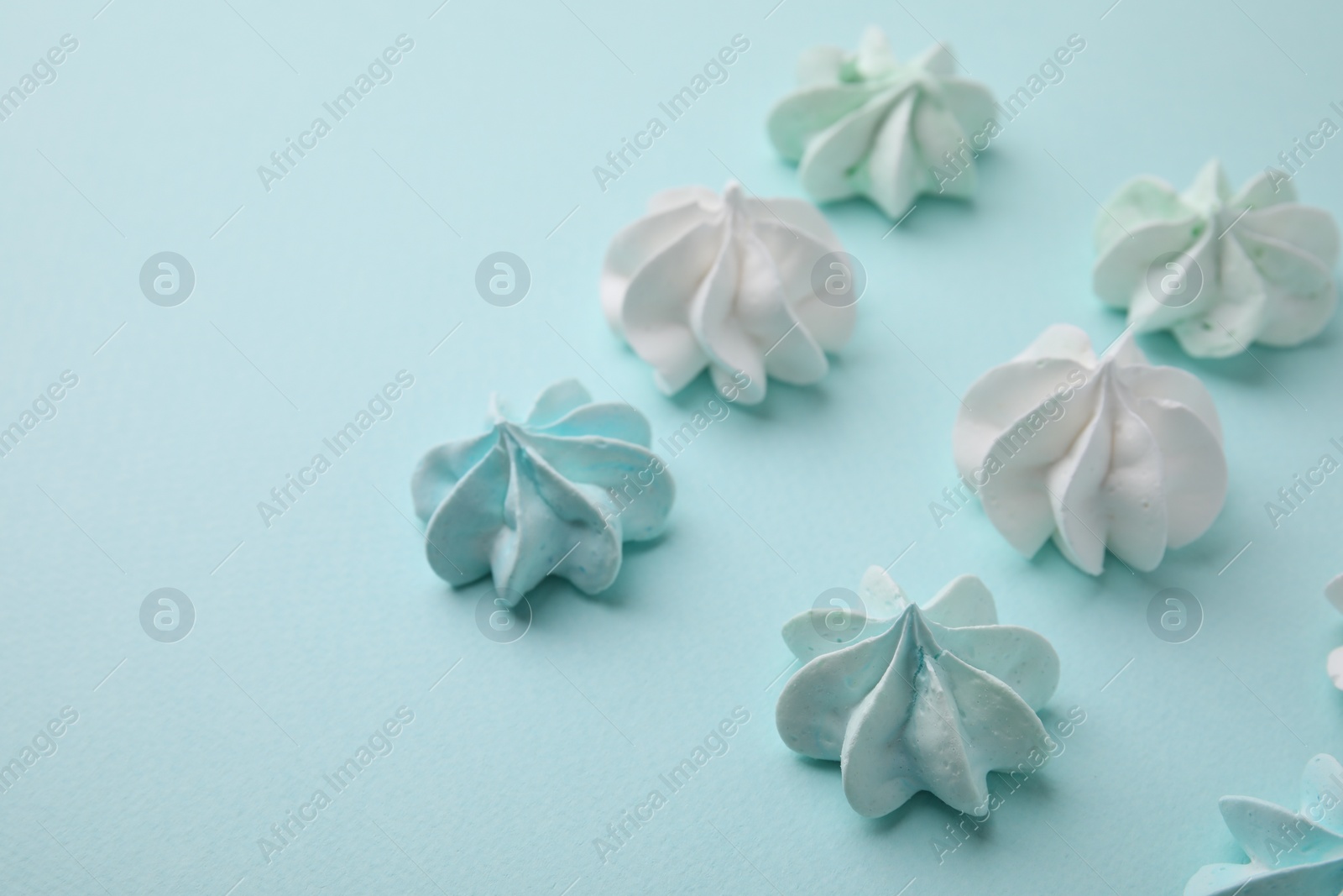 Photo of Delicious meringue cookies on light blue background, closeup. Space for text