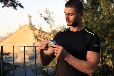 Photo of Attractive man checking pulse with blood pressure monitor on finger after training in park. Space for text