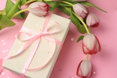Photo of Beautiful gift box with bow, tulips and confetti on pink background