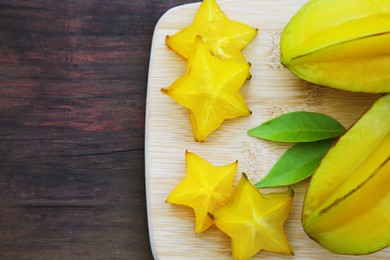 Photo of Delicious cut and whole carambolas with green leaves on wooden table, top view. Space for text