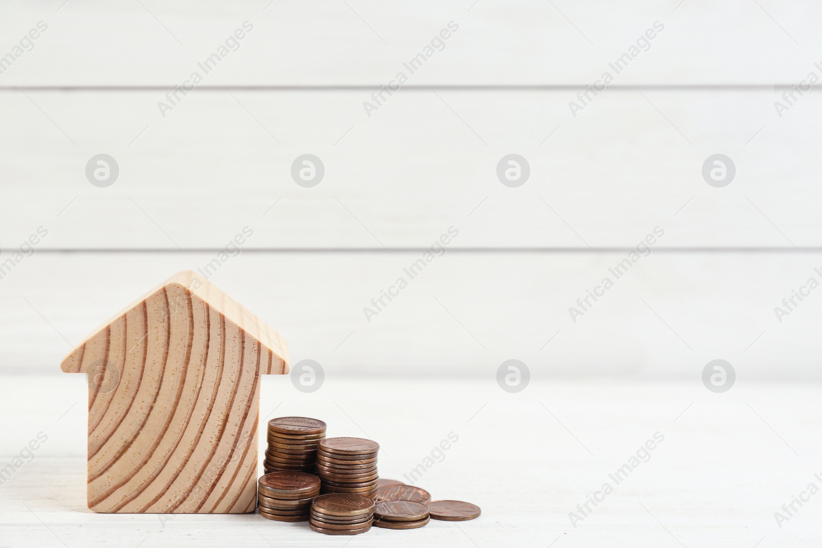 Photo of House model and coins on white wooden table. Space for text