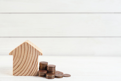 House model and coins on white wooden table. Space for text