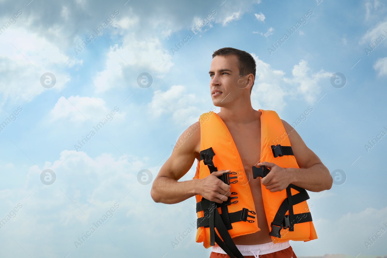 Photo of Handsome lifeguard putting on life vest against sky