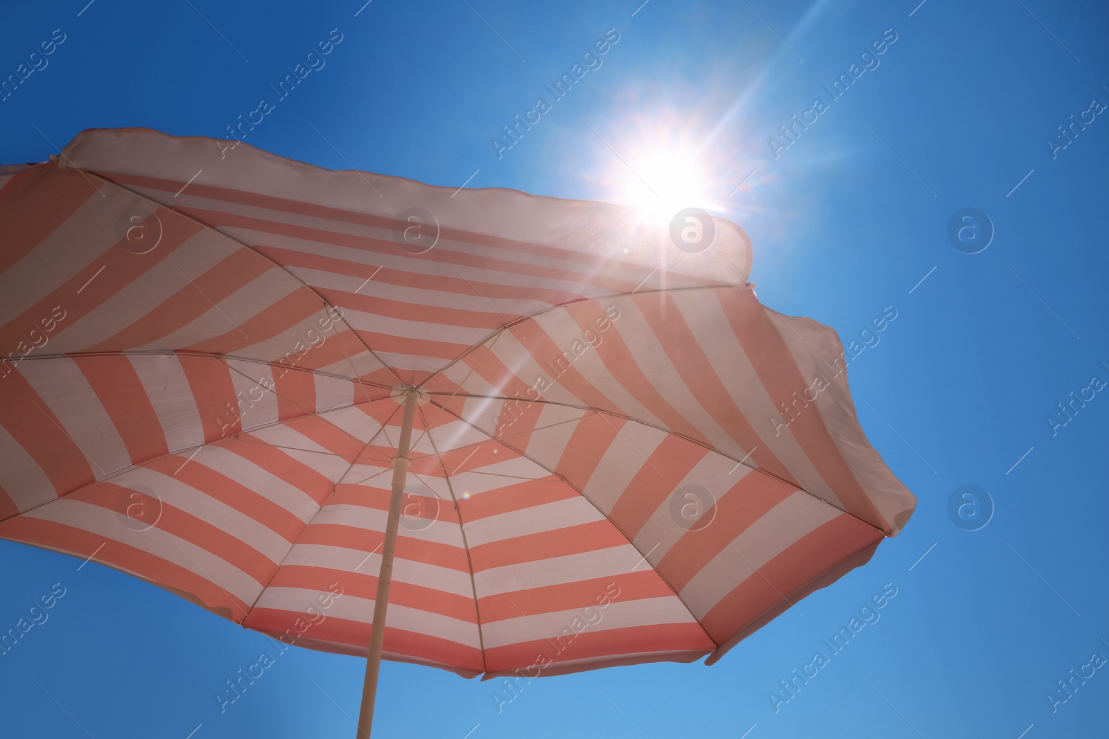 Photo of Red and white striped beach umbrella against blue sky on sunny day