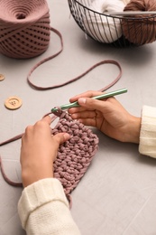 Photo of Woman crocheting with threads at grey table, closeup. Engaging hobby