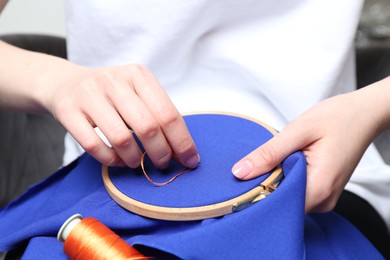 Photo of Woman with sewing needle and thread embroidering on cloth, closeup