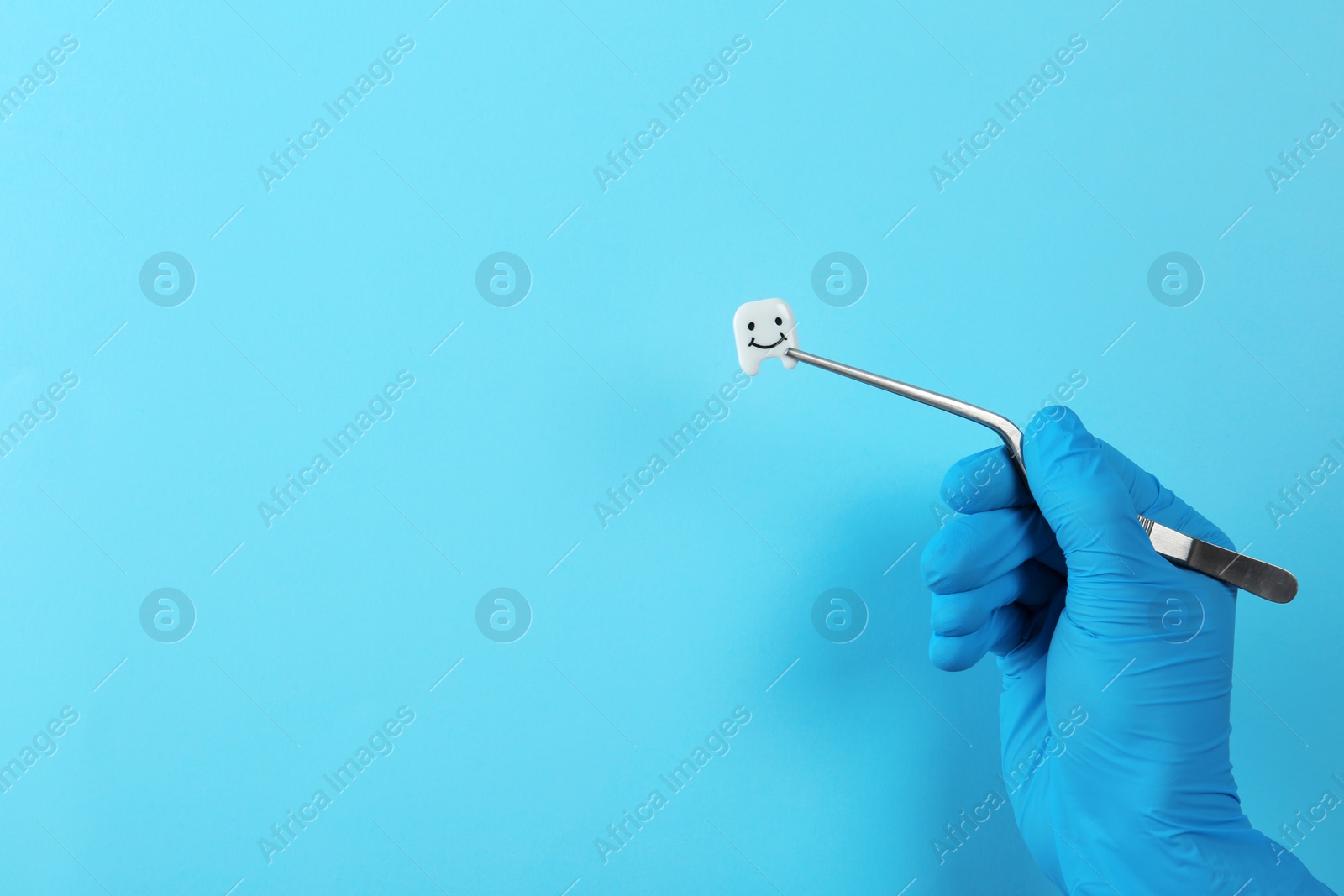 Photo of Dentist holding small plastic tooth with tweezers on color background. Space for text