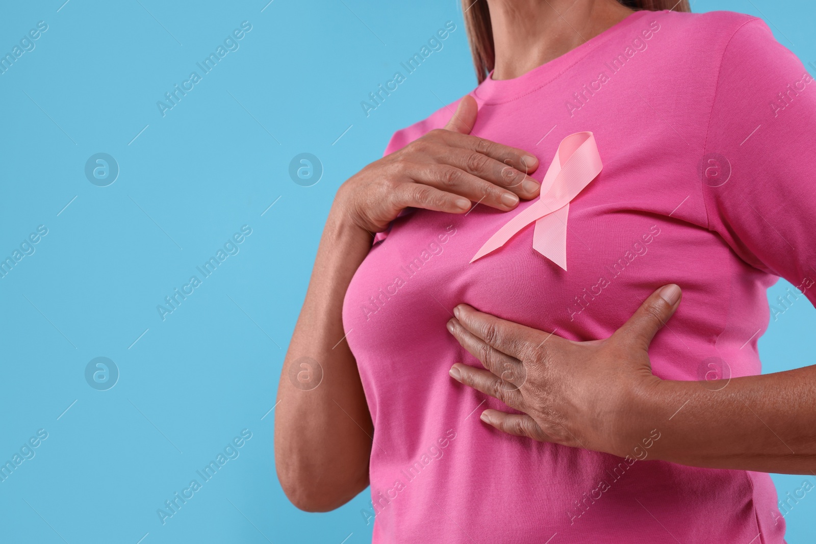 Photo of Woman with pink ribbon on light blue background, closeup and space for text. Breast cancer awareness