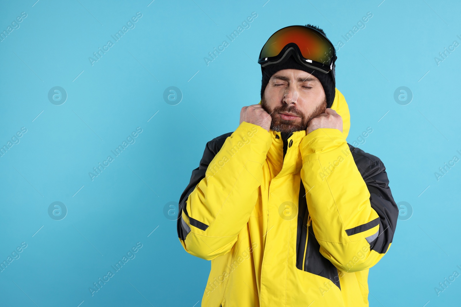 Photo of Winter sports. Man in ski suit and goggles on light blue background, space for text