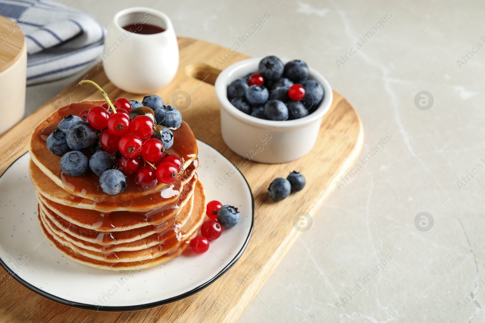 Photo of Delicious pancakes with fresh berries and syrup on light marble table