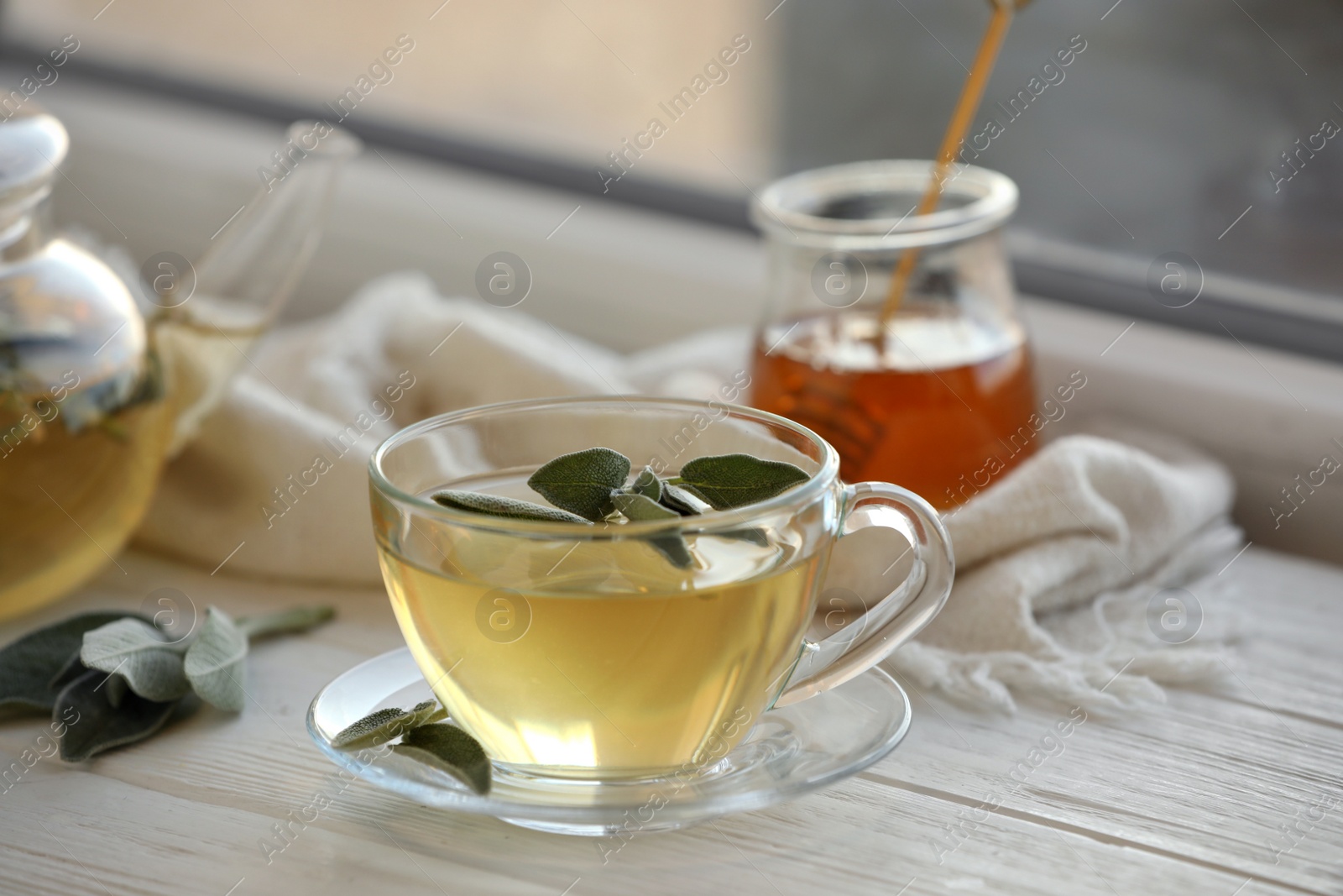 Photo of Cup of sage tea and green leaves on white wooden windowsill