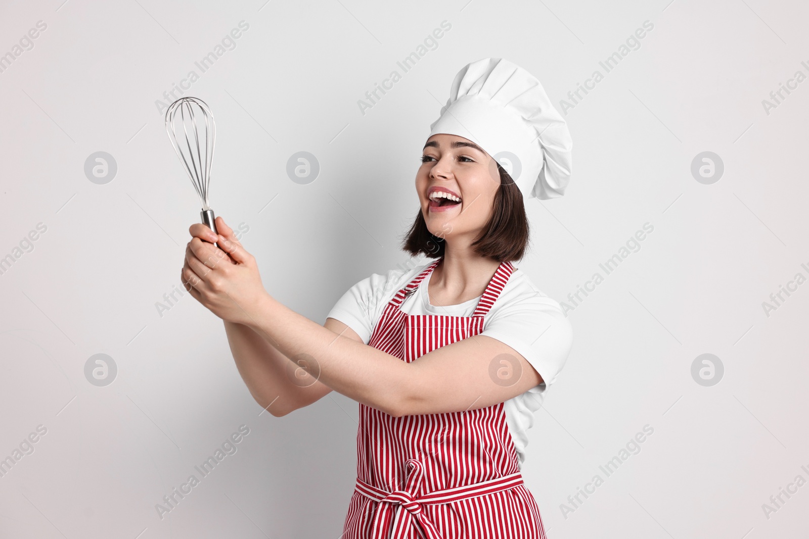 Photo of Happy confectioner holding whisk on light grey background