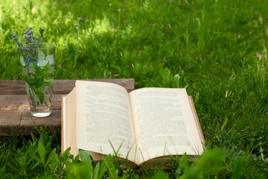 Photo of Open book with flowers in glass on green grass outdoors