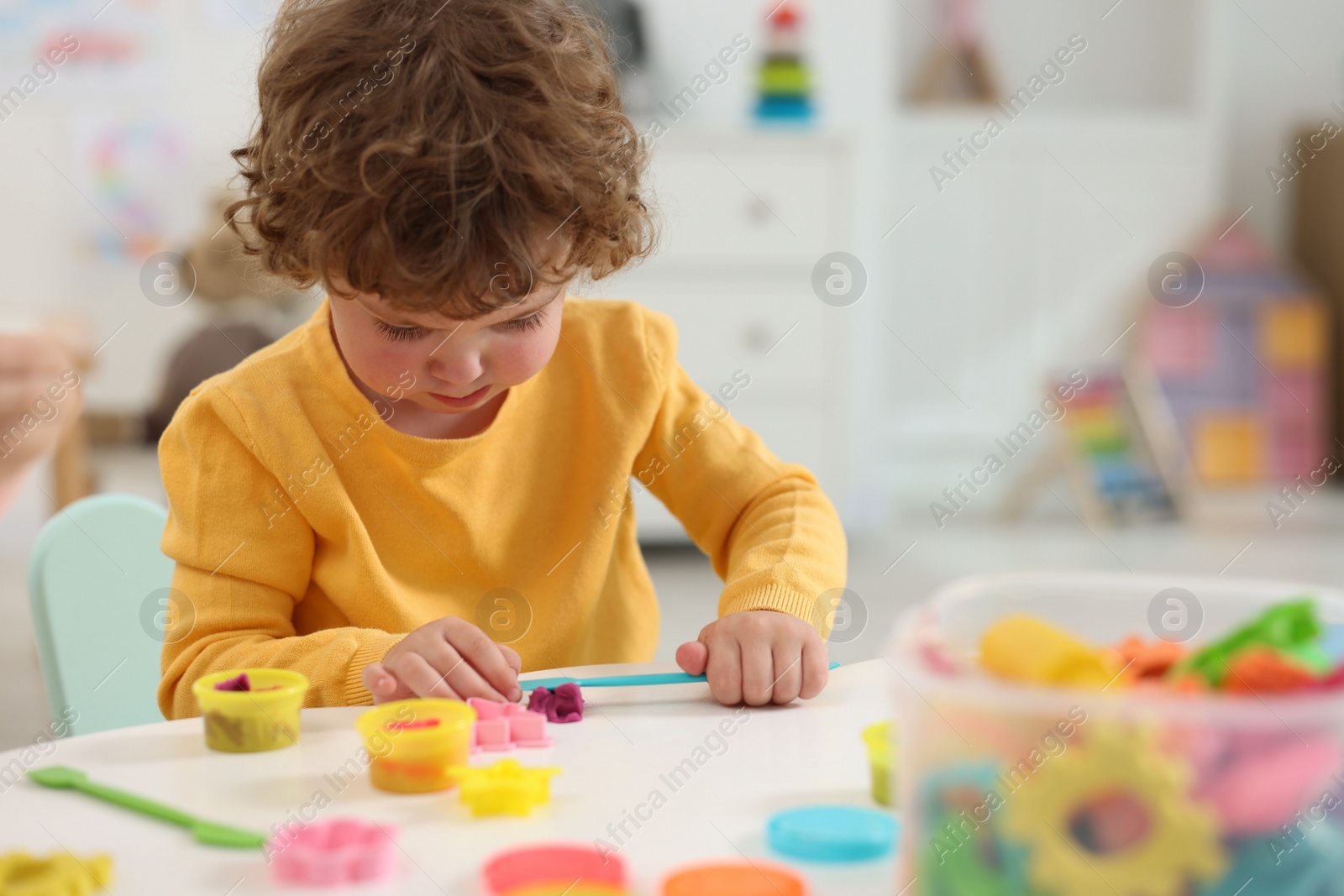 Photo of Cute little boy modeling from plasticine at white table in kindergarten. Space for text