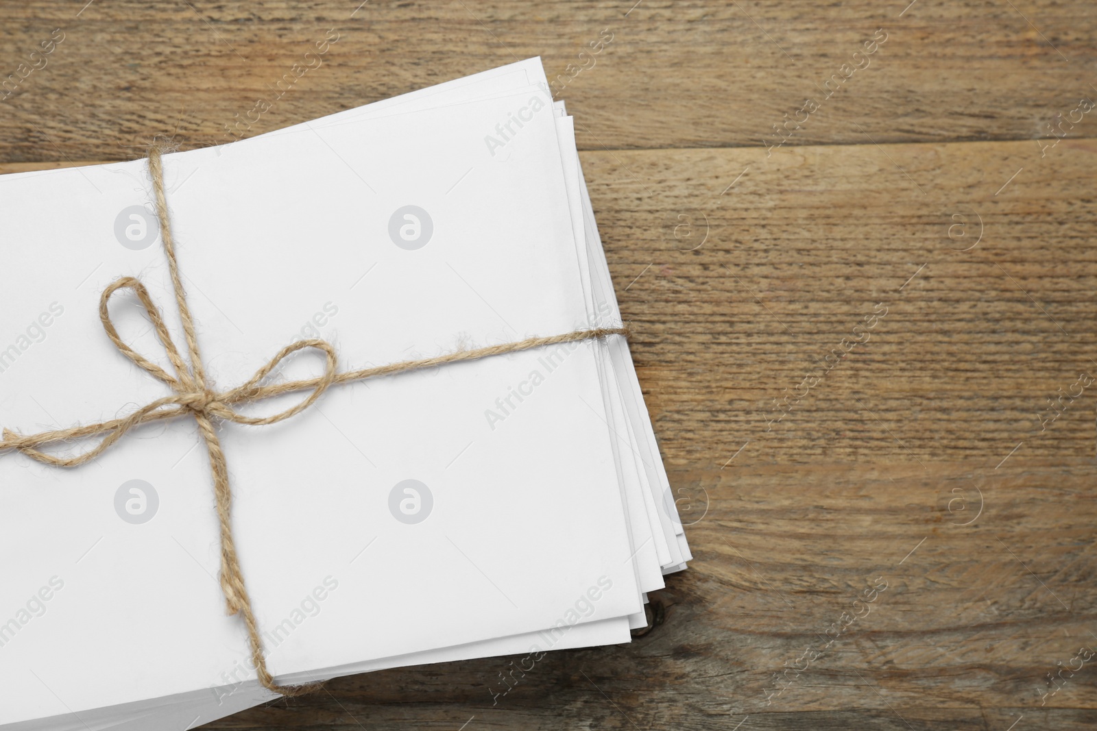 Photo of Stack of letters tied with twine on wooden table, top view. Space for text