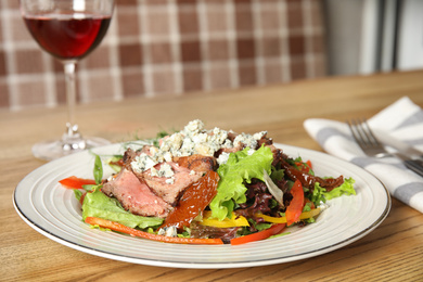 Photo of Delicious salad with roasted meat and vegetables served on wooden table indoors