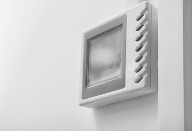 Photo of Modern thermostat on white wall. Heating system