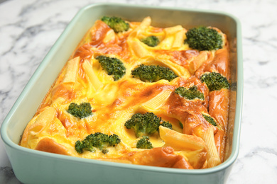 Tasty broccoli casserole in baking dish on white marble table, closeup