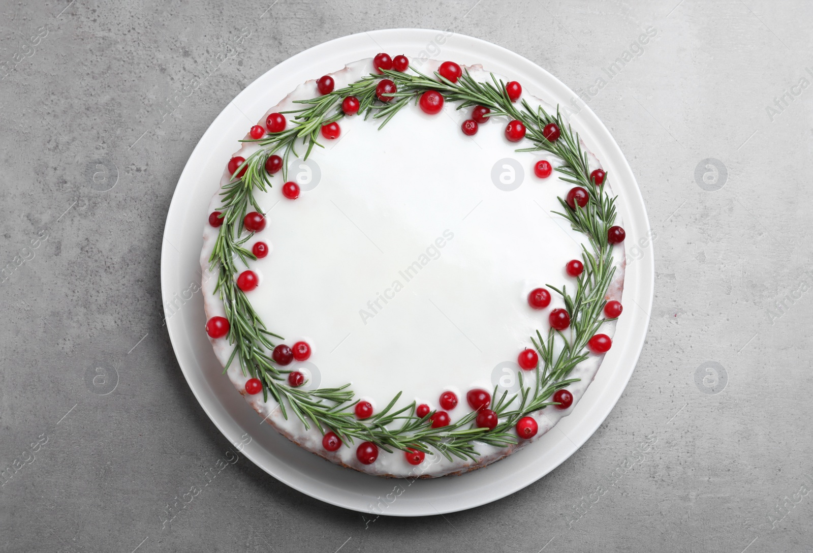 Photo of Traditional Christmas cake decorated with rosemary and cranberries on light grey table, top view