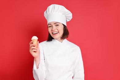 Photo of Happy confectioner with delicious ice cream cone on red background