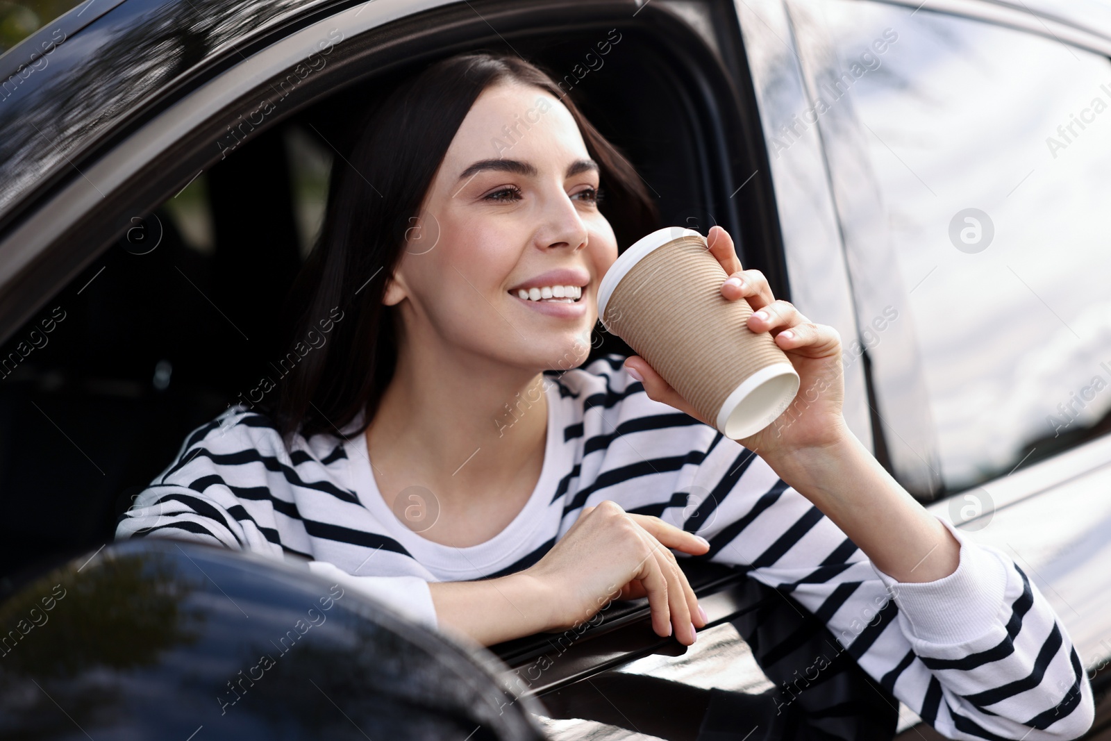 Photo of Young woman with cup of coffee sitting inside her modern car