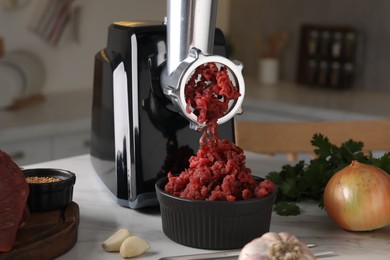 Photo of Electric meat grinder with beef mince and products on white marble table in kitchen