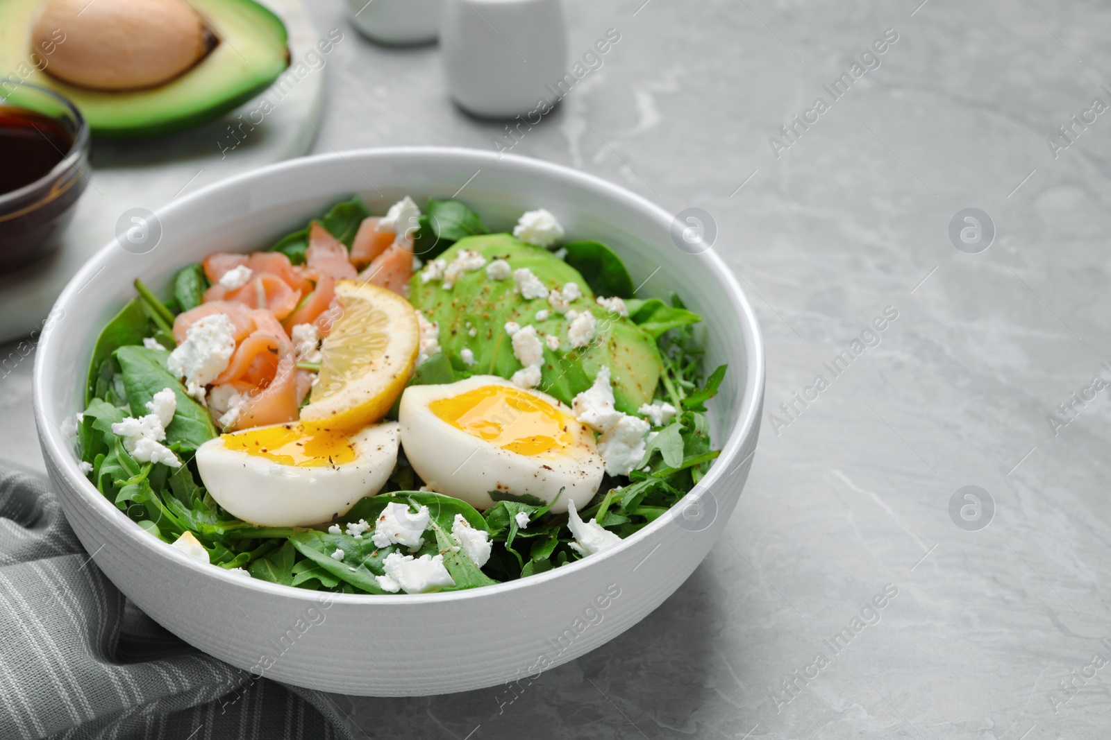 Photo of Delicious salad with boiled egg, salmon and cheese in bowl on light grey marble table