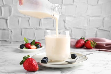 Woman pouring tasty yogurt into glass at white marble table, closeup