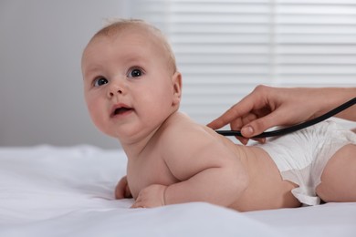 Pediatrician examining cute little baby with stethoscope in clinic, closeup