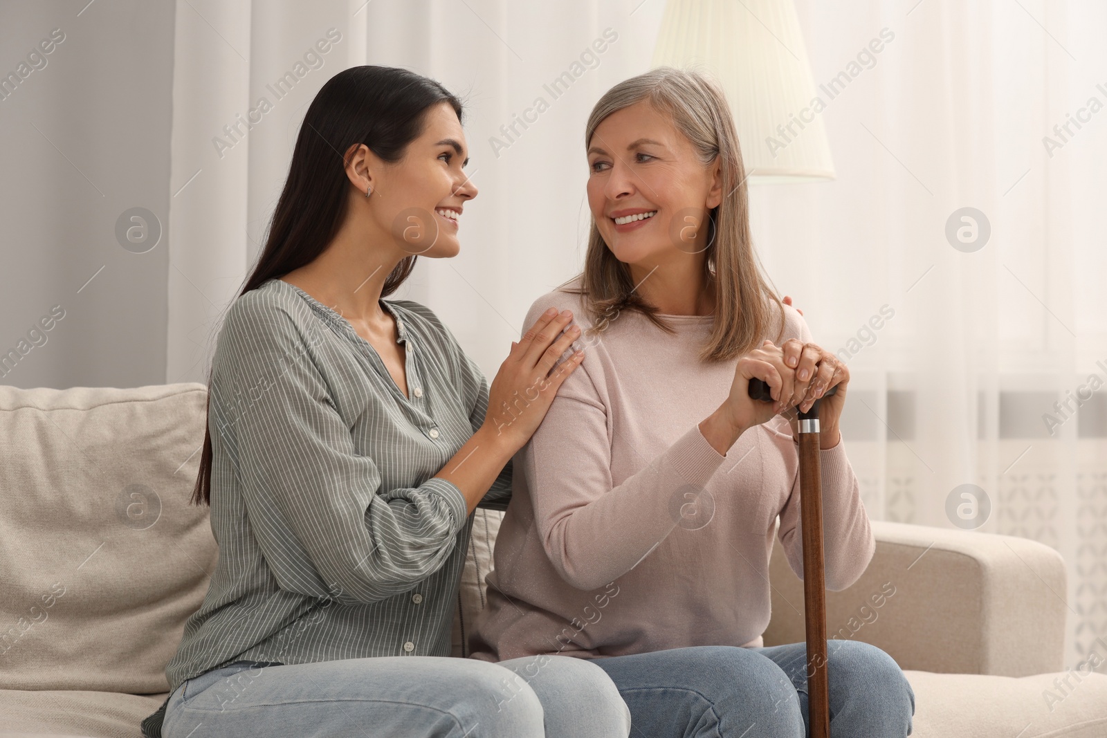 Photo of Mature lady with walking cane and young woman on sofa at home