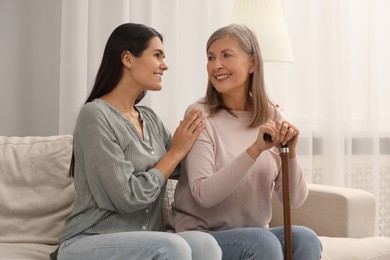 Mature lady with walking cane and young woman on sofa at home