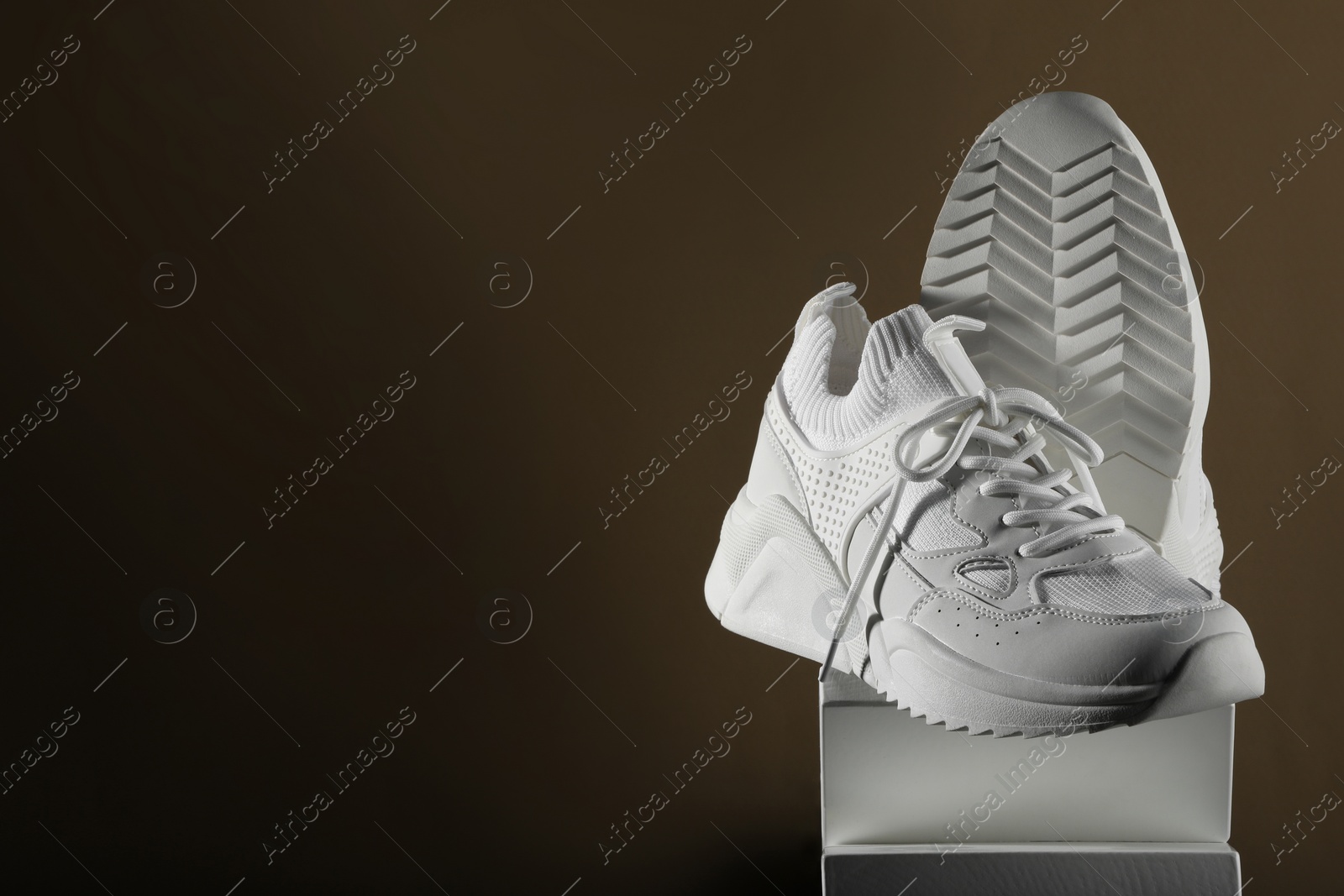 Photo of Pair of stylish white sneakers on brown background, space for text