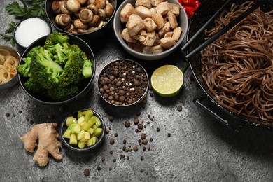 Wok with noodles, chicken and other products on grey table, above view