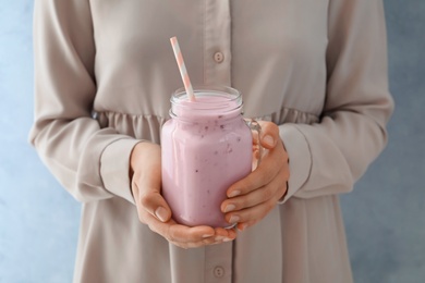 Photo of Woman holding mason jar with fig smoothie on light blue background, closeup