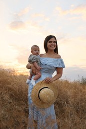 Happy mother with adorable baby in field at sunset