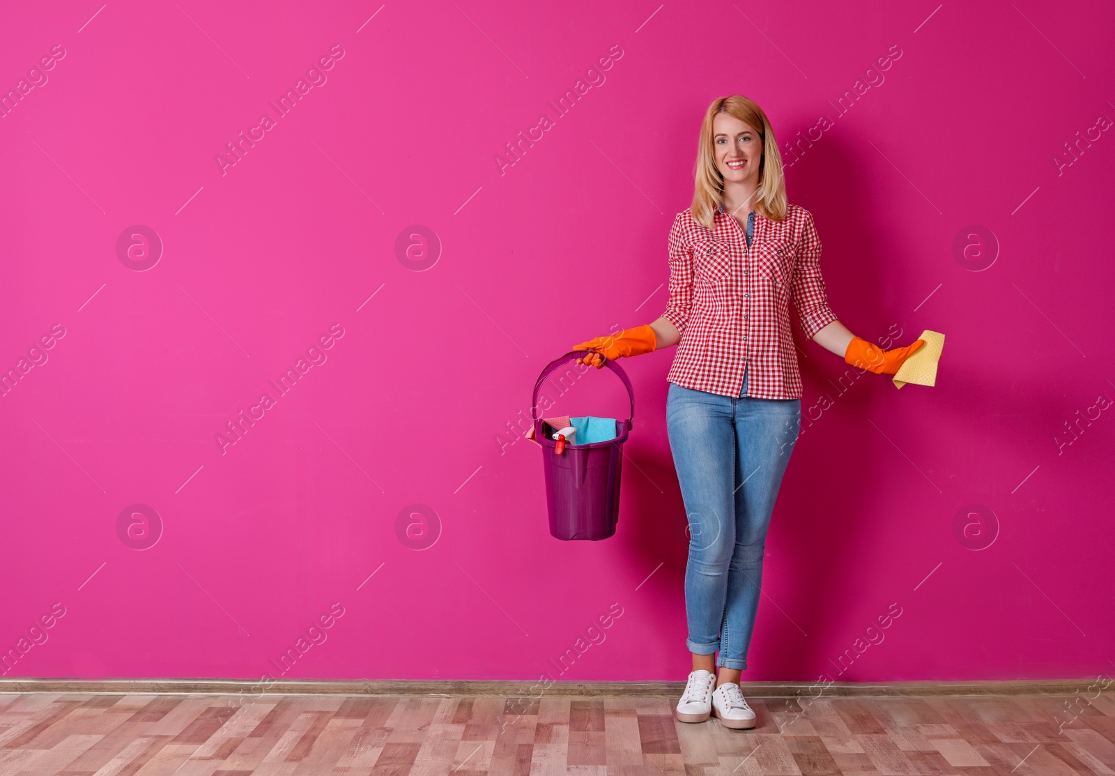 Photo of Woman with cleaning supplies near color wall