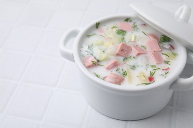 Photo of Delicious cold summer soup (okroshka) with boiled sausage in pot on white tiled table, closeup. Space for text