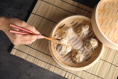 Photo of Woman cooking tasty baozi dumplings in bamboo steamer at table, top view