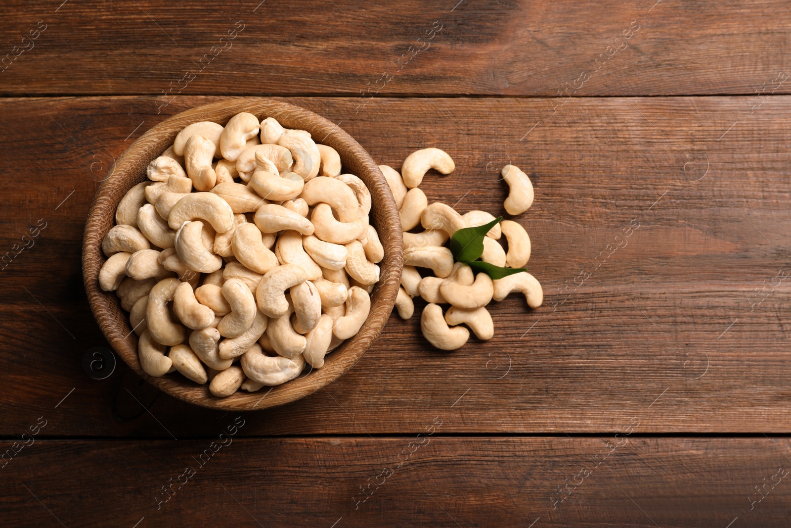 Photo of Tasty cashew nuts in bowl on wooden table, top view. Space for text