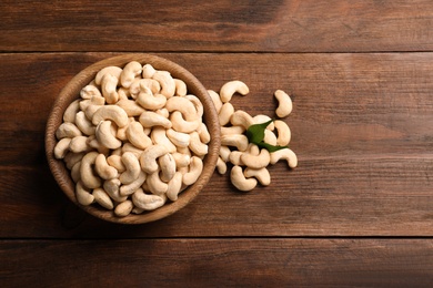 Photo of Tasty cashew nuts in bowl on wooden table, top view. Space for text
