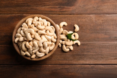 Tasty cashew nuts in bowl on wooden table, top view. Space for text