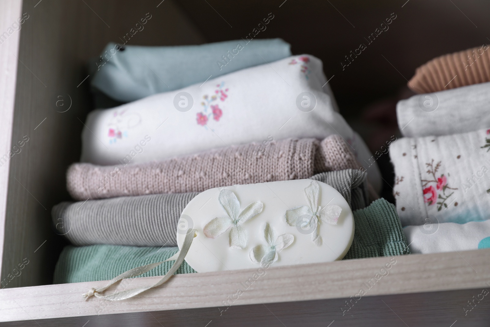 Photo of Beautiful scented wax sachet near stack of clothes on shelf in wardrobe, closeup