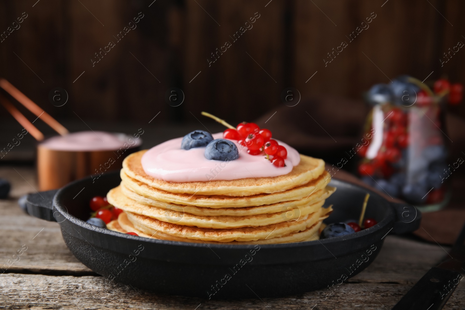 Photo of Tasty pancakes with natural yogurt, blueberries and red currants on wooden table