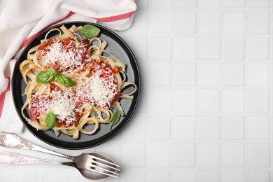 Delicious pasta with tomato sauce, basil and parmesan cheese on white tiled table, flat lay. Space for text