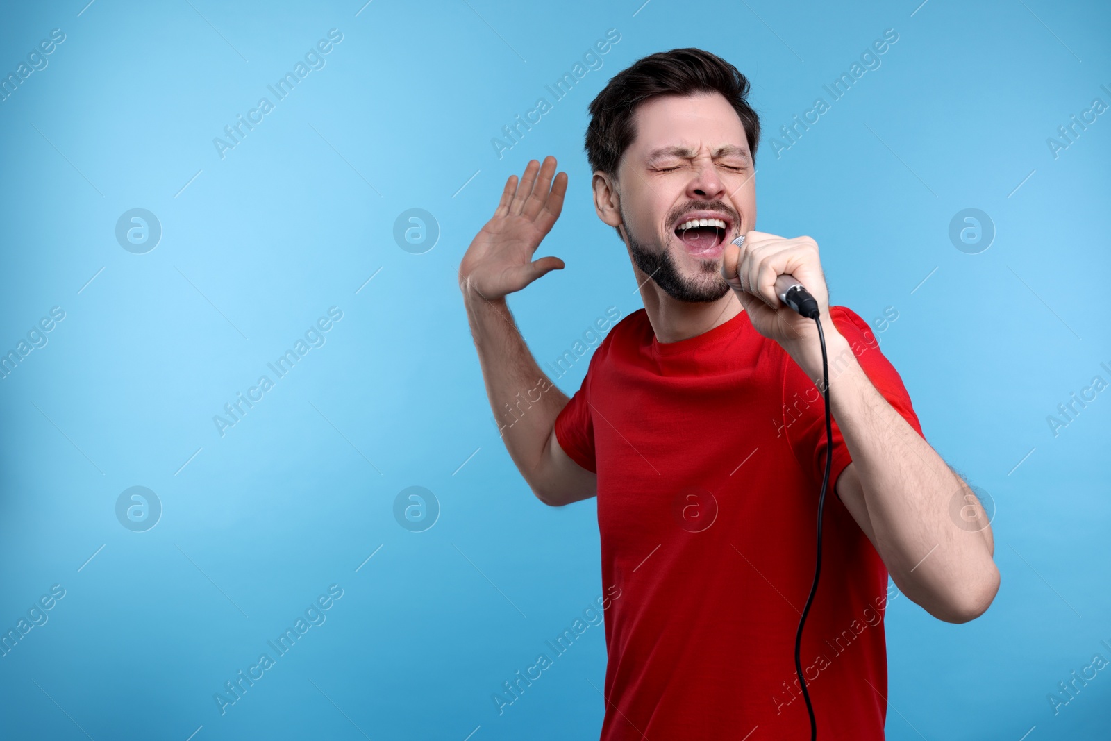 Photo of Handsome man with microphone singing on light blue background. Space for text