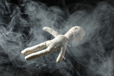Photo of Voodoo doll with pins and smoke on dark background