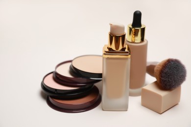 Photo of Face powders, foundations and makeup brush on light background, closeup
