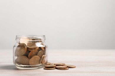 Photo of Glass jar with coins on white wooden table. Space for text