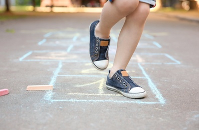 Little child playing hopscotch drawn with colorful chalk on asphalt